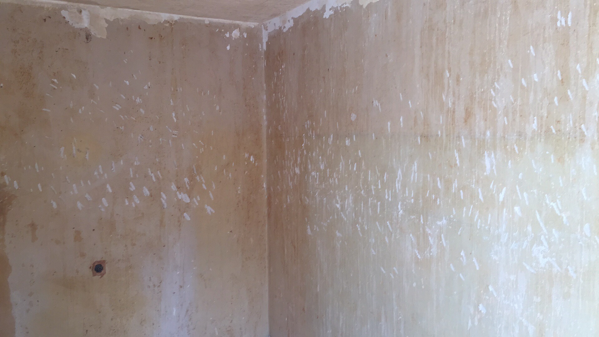 Przygotowanie ścian do malowania: zdarte fragmenty starej farby i ślady szpachlowania na ścianach w rogu pomieszczenia.