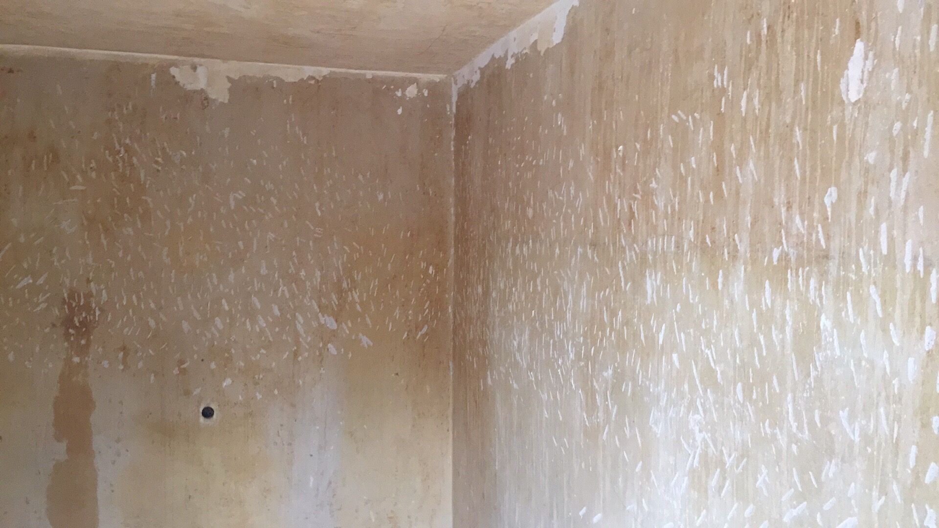 Pokój w trakcie przygotowania do malowania: zdarte fragmenty starej farby i tapety na ścianach, widoczny otwór po gwoździu.