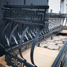 Elementy balustrady balkonowej z motywem greckim, pomalowane proszkowo na grafitowy kolor, czekają na montaż.