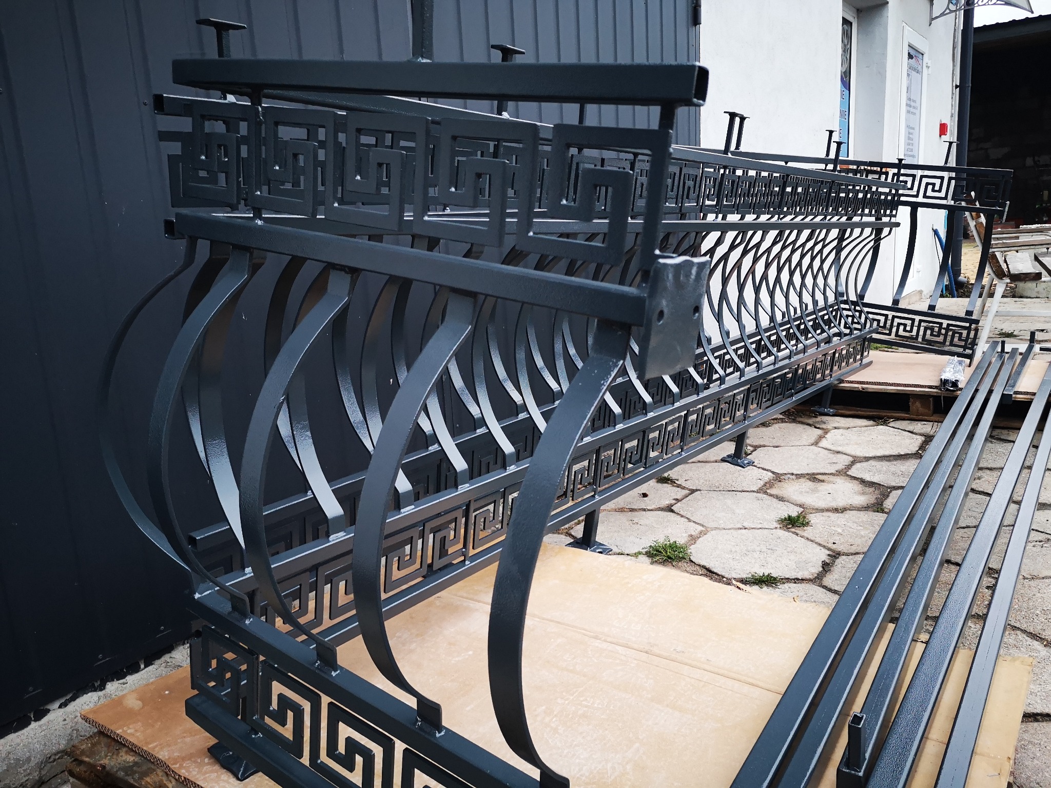 Elementy balustrady balkonowej z motywem greckim, pomalowane proszkowo na grafitowy kolor, czekają na montaż.