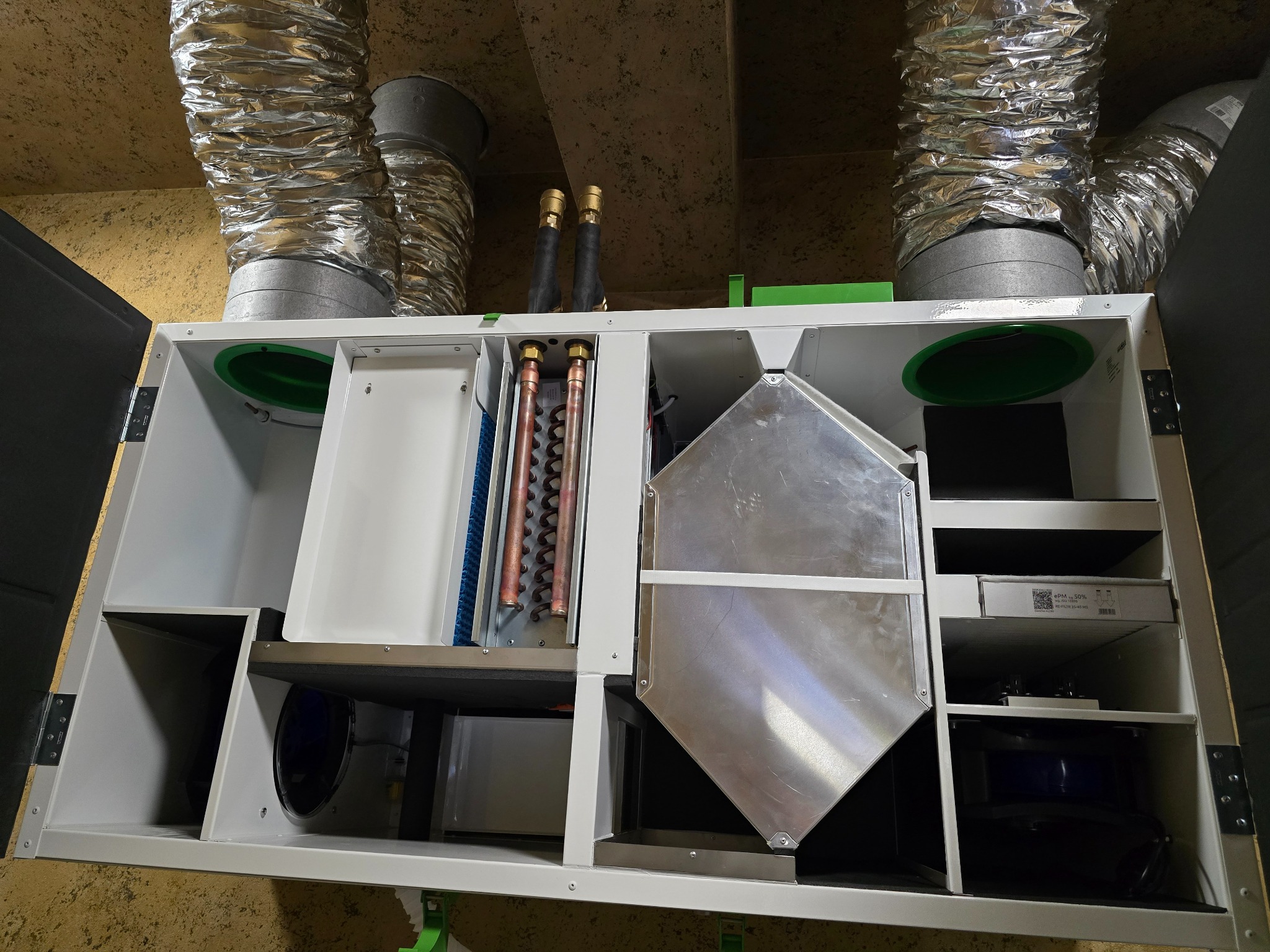 Centrala wentylacyjna z rekuperacją, widoczne kanały wentylacyjne i elementy wewnętrzne, takie jak wymiennik ciepła i filtry. Montaż w pomieszczeniu technicznym.