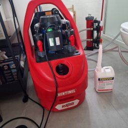 Zakład instalacyjny wod-kan i C.O. Rafał Walter - Czerwona pompa Sentinel JetFlush Rapid z płynem Fernox DS40, do czyszczenia instalacji grzewczych, widoczna w łazience z elementami instalacji hydrauliczej.