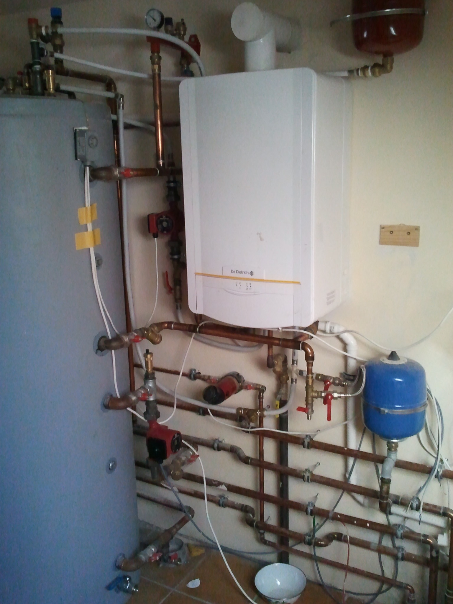 Kompleksowa instalacja grzewcza z piecem De Dietrich, zbiornikiem i licznymi rurami miedzianymi, zaworami oraz pompami obiegowymi w pomieszczeniu technicznym.