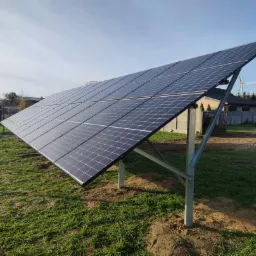 Panel słoneczny na metalowej konstrukcji, zainstalowany na trawniku przed domem jednorodzinnym w słoneczny dzień.