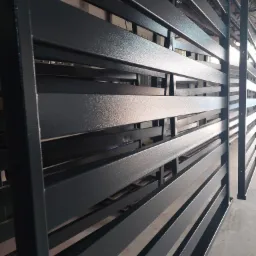 Metalowa konstrukcja z poziomymi listwami pomalowana na ciemny szary kolor z widoczną fakturą, prawdopodobnie pomalowana proszkowo.