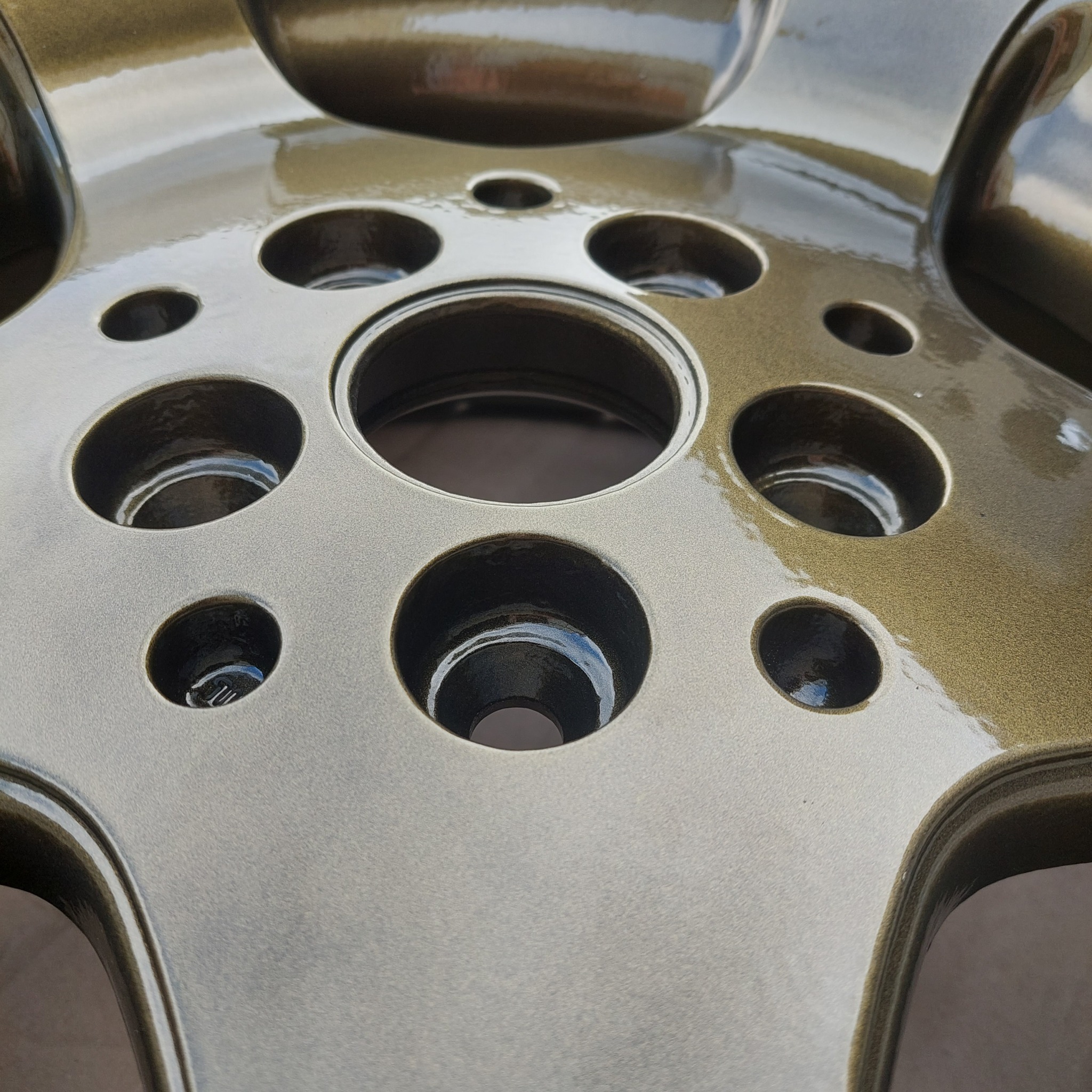 Błyszcząca, złoto-brązowa felga aluminiowa z licznymi otworami, po renowacji i nowym lakierowaniu, widoczna z bliska pod kątem.