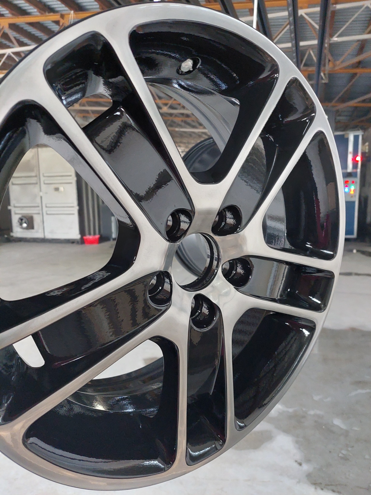 Błyszcząca felga samochodowa po malowaniu proszkowym, widoczne srebrne i czarne wykończenie, w tle maszyny lakiernicze.
