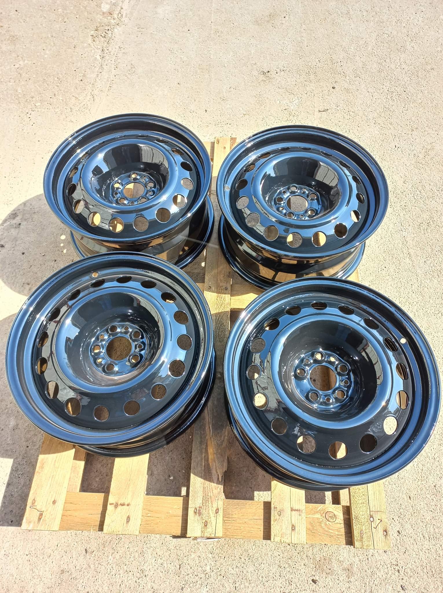 Cztery czarne felgi samochodowe po renowacji, ułożone na drewnianej palecie w Trzebiatowie, z wyraźnym odbiciem światła na powierzchni.