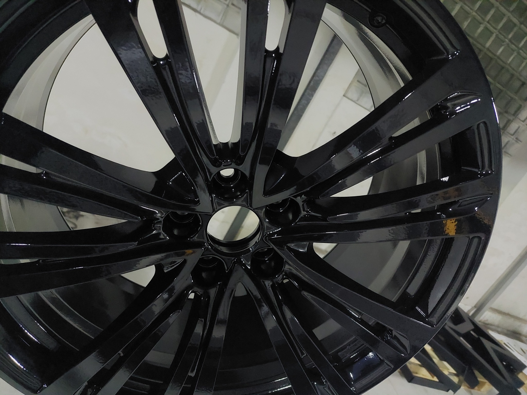 Błyszcząca, czarna felga aluminiowa z widocznymi refleksami światła, ustawiona pod kątem w warsztacie.