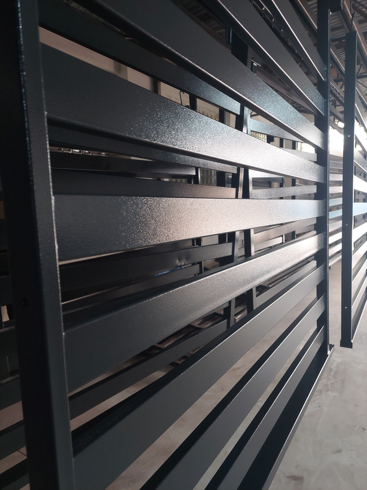 Metalowa konstrukcja z poziomymi listwami pomalowana na ciemny szary kolor z widoczną fakturą, prawdopodobnie pomalowana proszkowo.