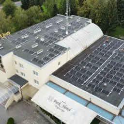 Widok z lotu ptaka na budynek hotelu z panelami słonecznymi na dachu, otoczony zielenią i drzewami.