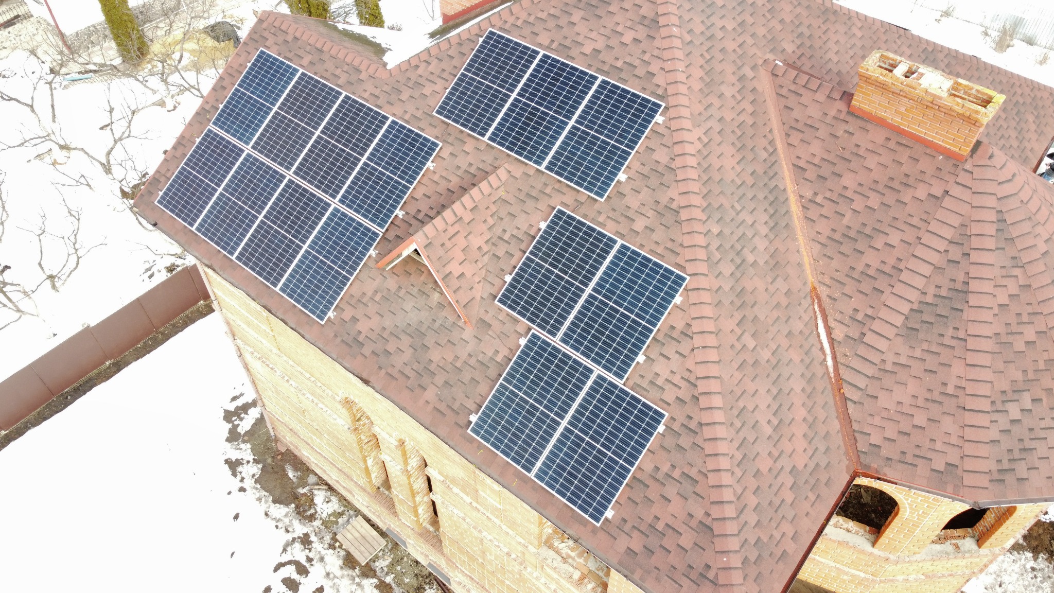 Widok z góry na panele fotowoltaiczne zamontowane na dachu domu z cegły w zimowej scenerii.