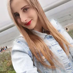 Portret młodej kobiety w jeansowej kurtce z czerwonymi ustami na tle plaży i morza.