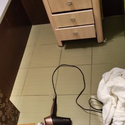 Agnieszka Gutman - Łazienka przed sprzątaniem: na podłodze leżą ubrania, suszarka Remington, ręcznik, obok umywalki z szafką.