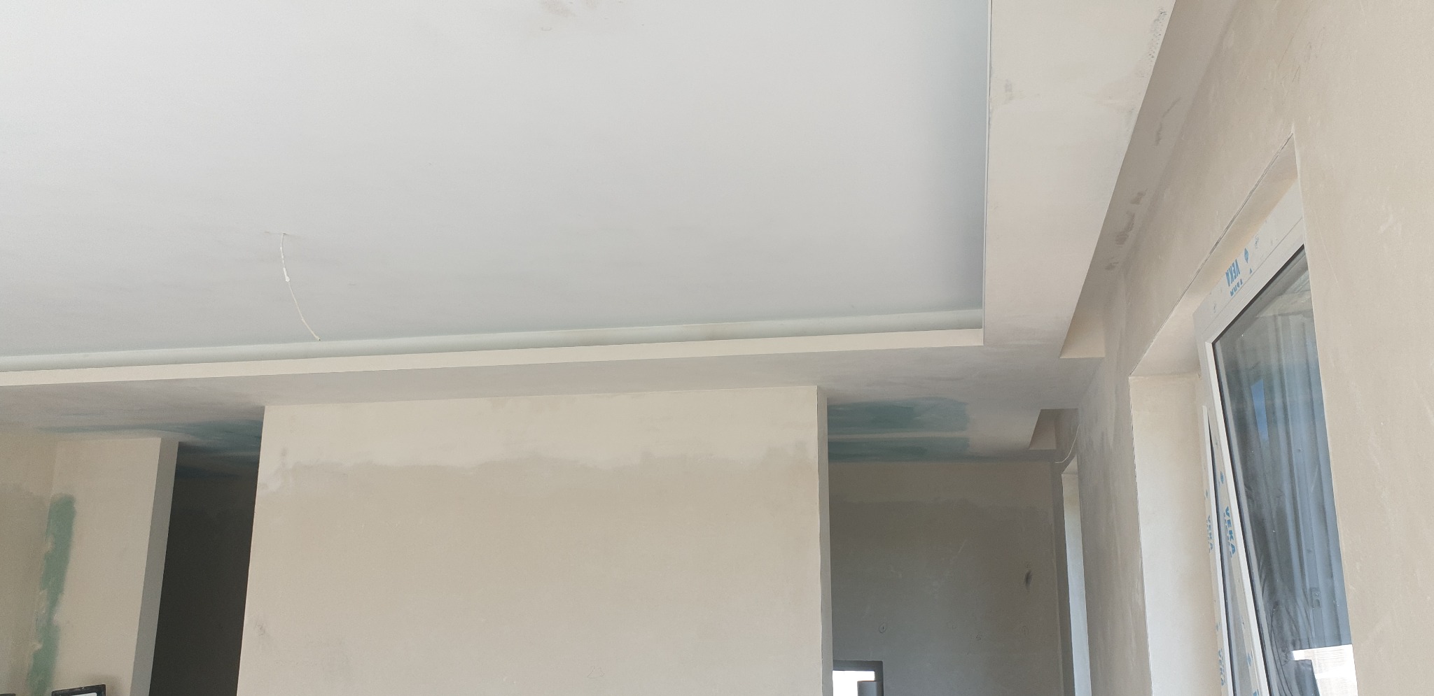 Wnętrze w trakcie remontu: sufit z elementami dekoracyjnymi, ściany po szpachlowaniu, widoczne okno i otwory drzwiowe