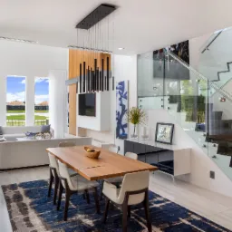 Nowoczesne wnętrze domu z balustradą szklaną na schodach, drewnianym stołem jadalnym i widokiem na jezioro przez okna.