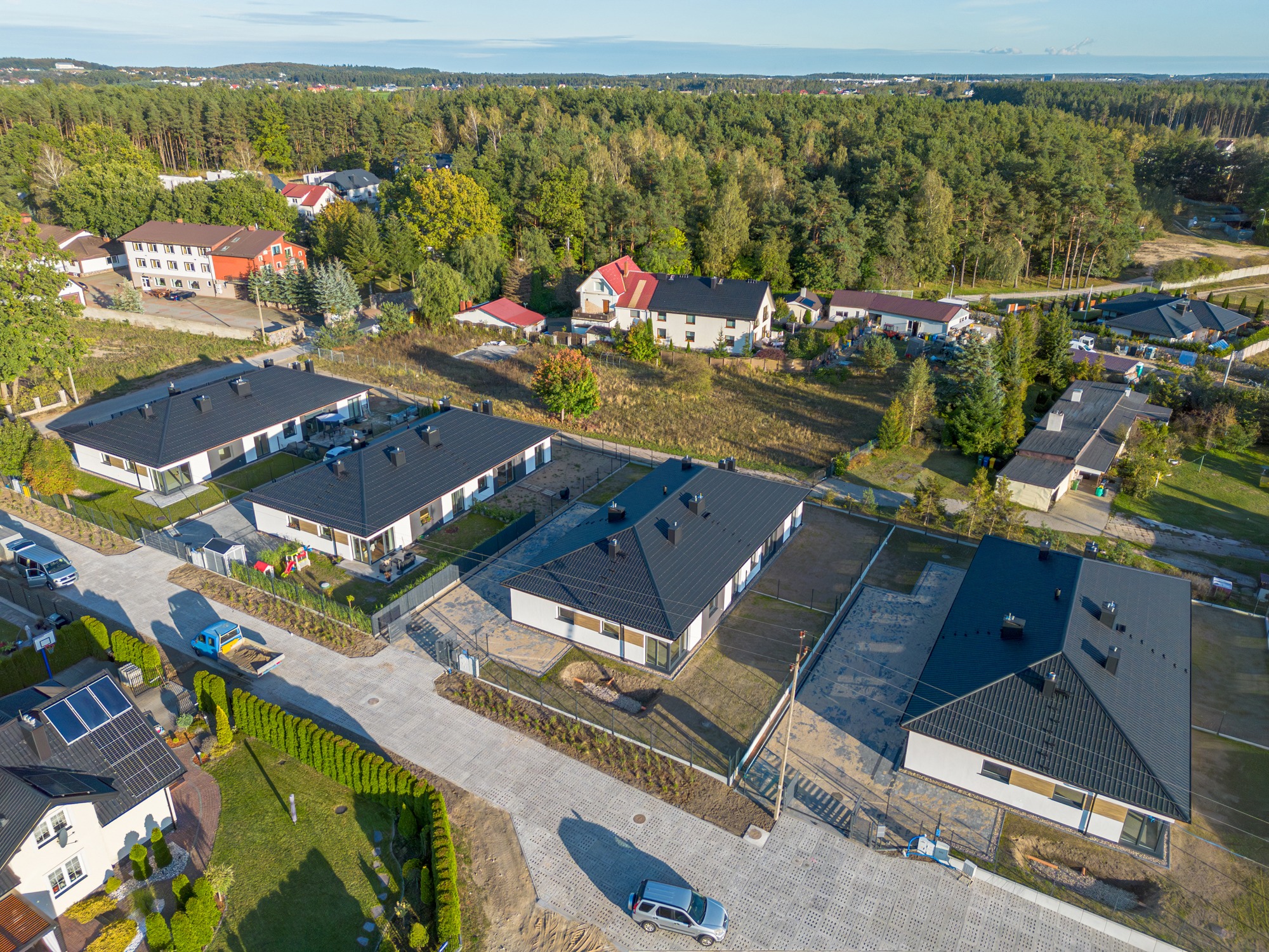 Widok z drona na osiedle domów jednorodzinnych z czarnymi dachami, szarą kostką brukową i zielenią. Domy w stylu nowoczesnym, z ogrodzeniami i zagospodarowanym terenem.