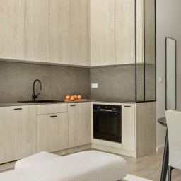 bajzel studio - Jasna, nowoczesna kuchnia z drewnianymi frontami szafek i czarną armaturą w Gliwicach. Na blacie leżą pomarańcze, a w tle widoczny fragment sofy.