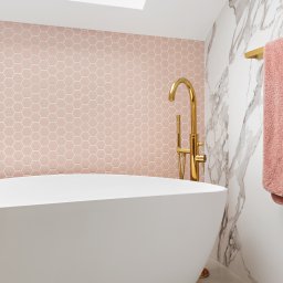 bajzel studio - Nowoczesna łazienka z wolnostojącą białą wanną, złotą armaturą i różową mozaiką heksagonalną na ścianie akcentującej, doświetlona oknem dachowym.