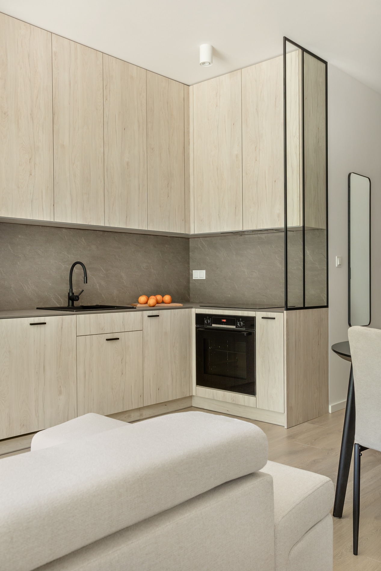 Jasna, nowoczesna kuchnia z drewnianymi frontami szafek i czarną armaturą w Gliwicach. Na blacie leżą pomarańcze, a w tle widoczny fragment sofy.