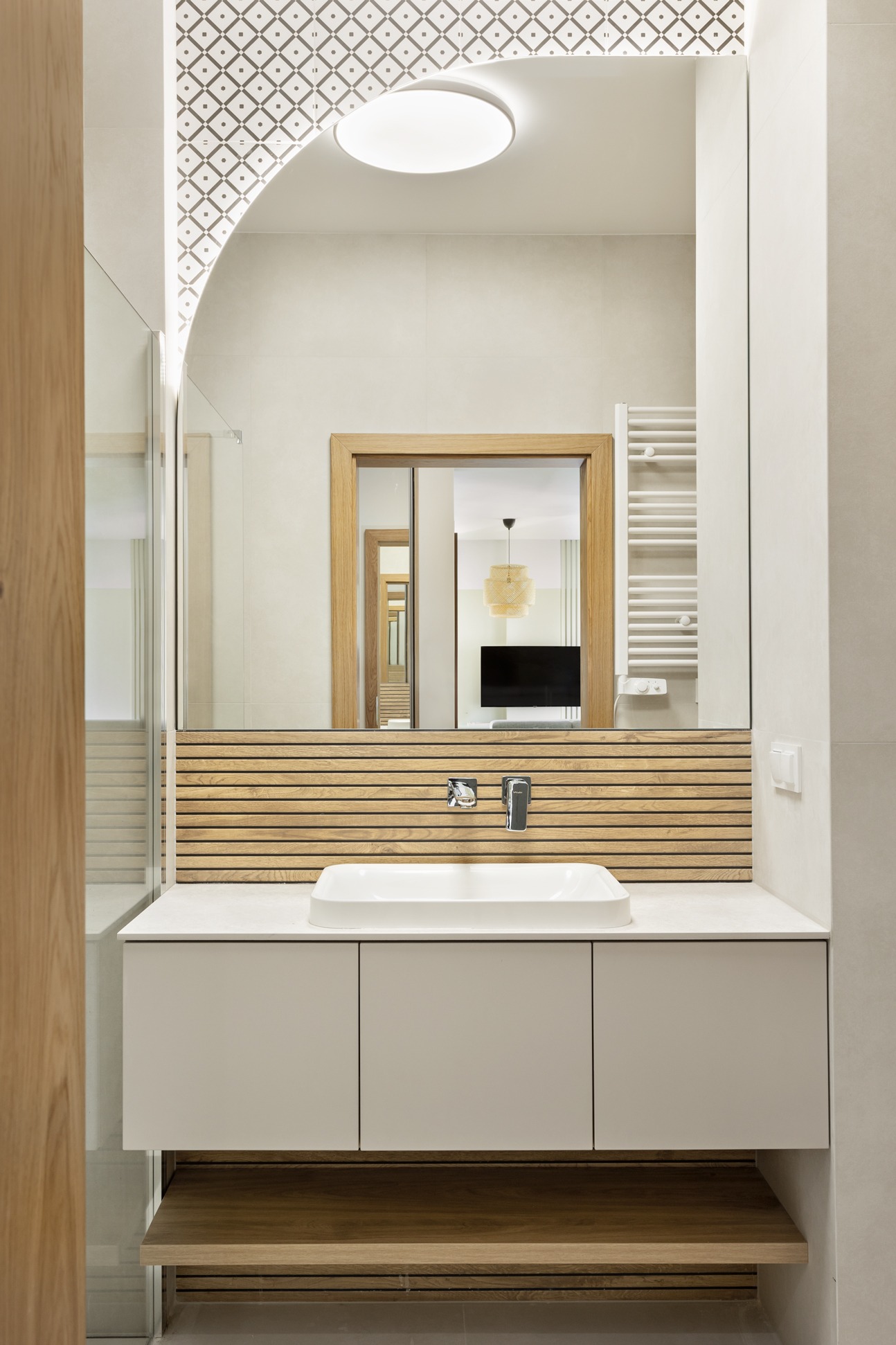 Nowoczesna łazienka z umywalką nablatową, drewnianymi lamelami za baterią i dużym lustrem z podświetlanym wzorem na suficie.