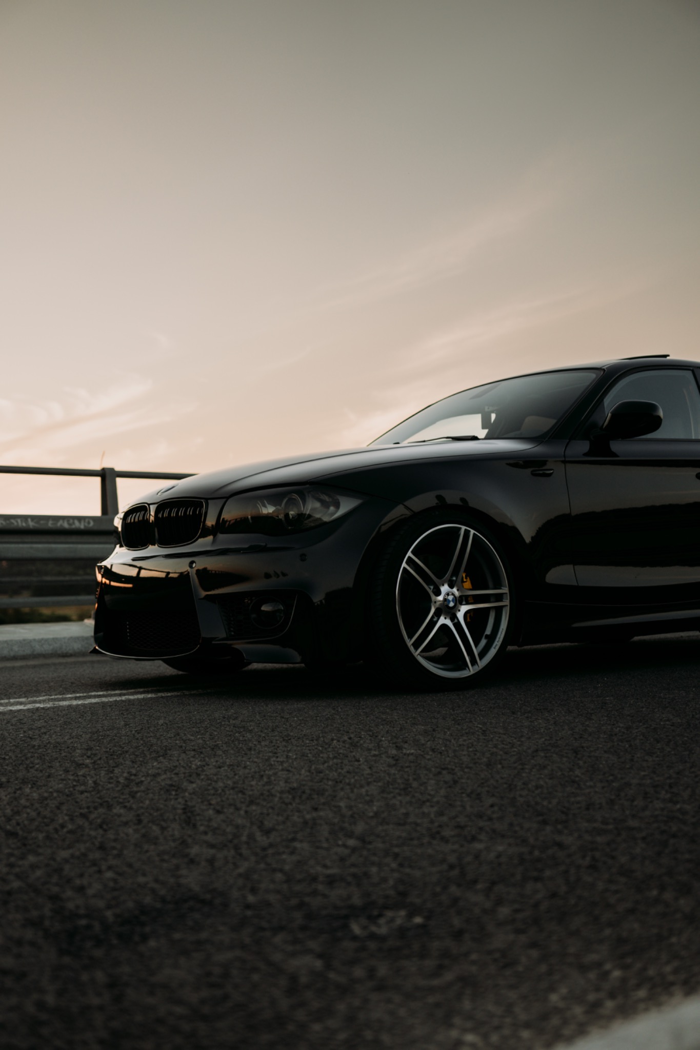Czarny samochód BMW serii 1 na tle zachodzącego słońca, widok z boku, felgi aluminiowe