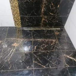 Wykończona podłoga w łazience z czarnych płytek imitujących marmur z złotymi żyłami, widoczny odpływ liniowy i fragment ściany z mozaiką w odcieniach złota i bieli.