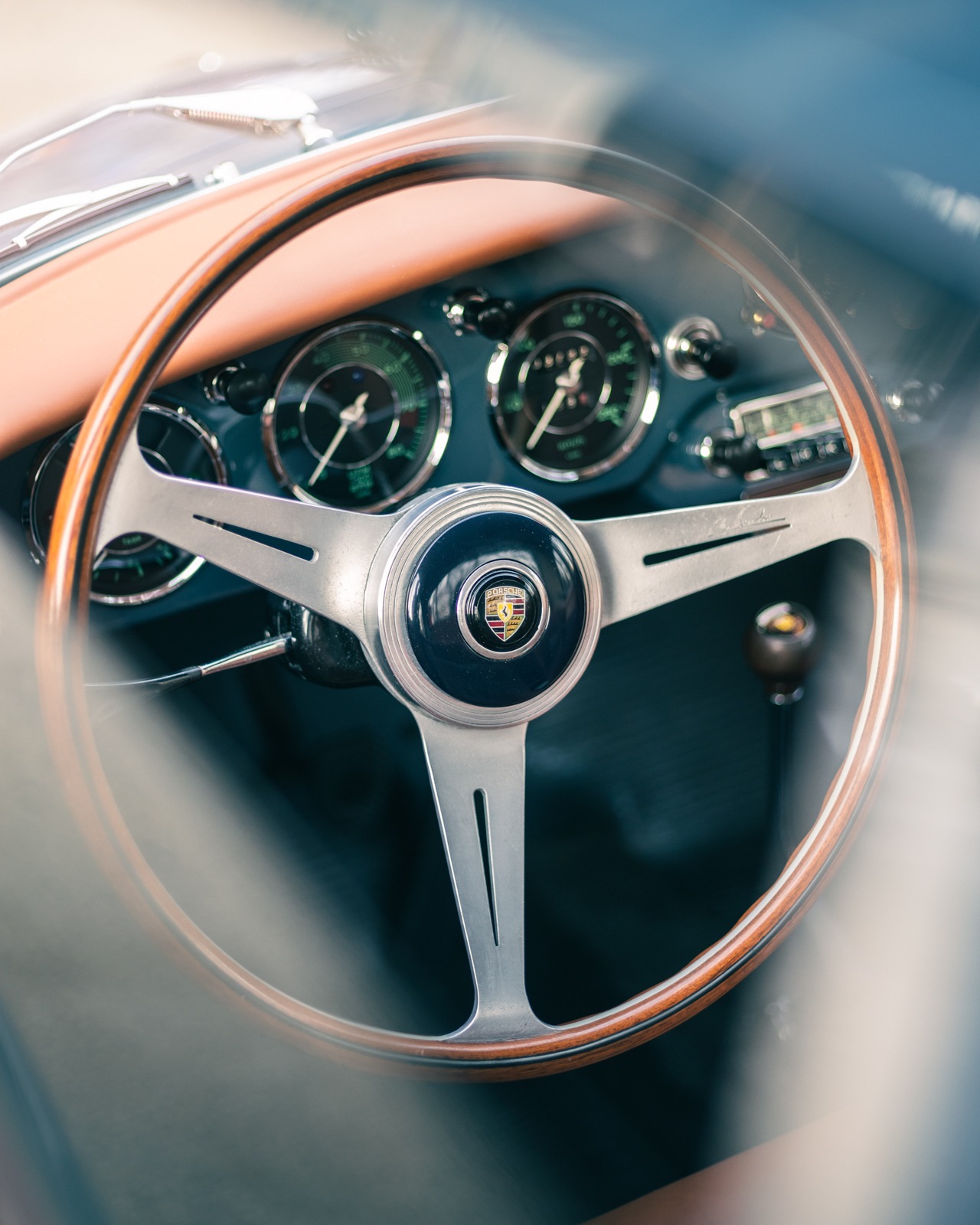 Wnętrze klasycznego samochodu Porsche 356: drewniana kierownica, srebrne ramiona, logo na środku, deska rozdzielcza z zielonymi wskaźnikami, radio.