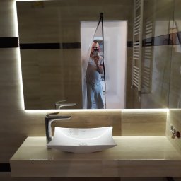 OLVIT - Nowoczesna łazienka z podświetlanym lustrem, umywalką w kształcie łodzi i grzejnikiem drabinkowym, widoczna osoba robiąca zdjęcie w lustrze.