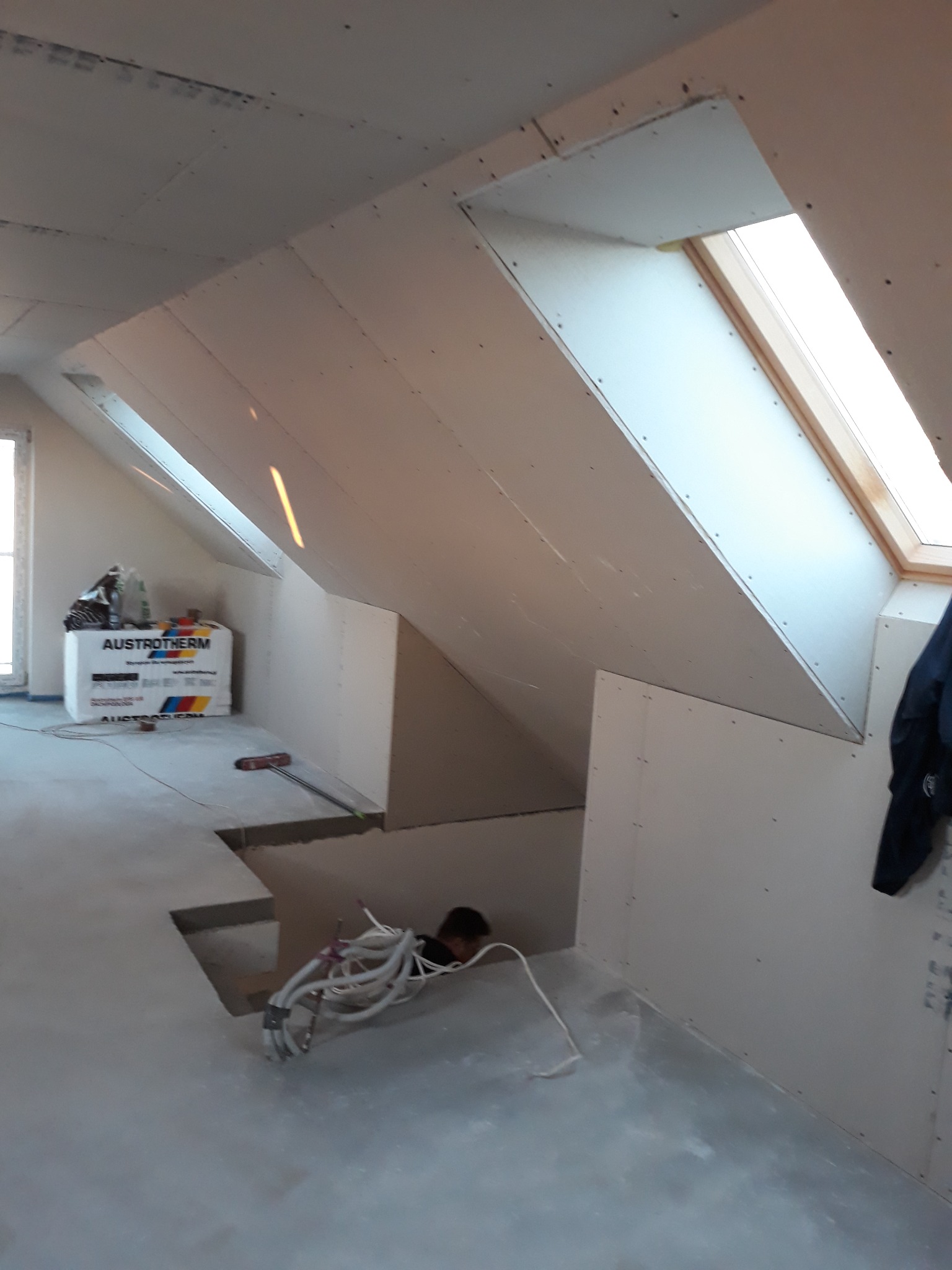 Poddasze w trakcie zabudowy płytami gipsowo-kartonowymi, widoczne okno dachowe, izolacja Austrotherm i przewody elektryczne wystające z otworu w podłodze.