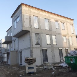 Przedsiębiorstwo Budowlane WB S.C Michał Wronkowski Łukasz Boczoń - Wznoszony trzypiętrowy dom murowany z keramzytobetonu z widoczną konstrukcją balkonu, zabezpieczonymi oknami folią, paletą bloczków Sil-Pro i kontenerem na gruz.