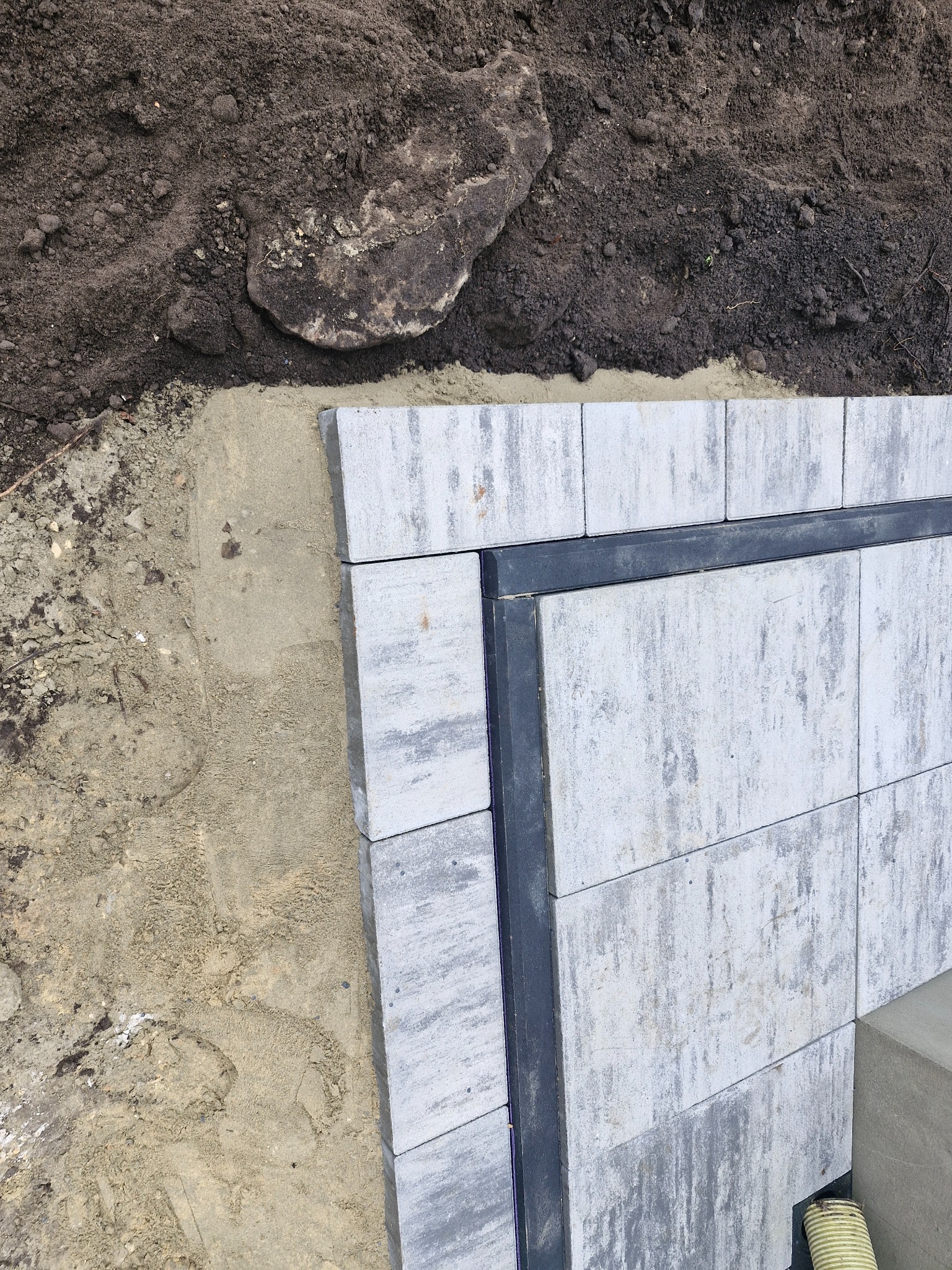 Fragment konstrukcji tarasu z szarych płyt betonowych, widoczne przygotowane podłoże z piasku i ziemi.