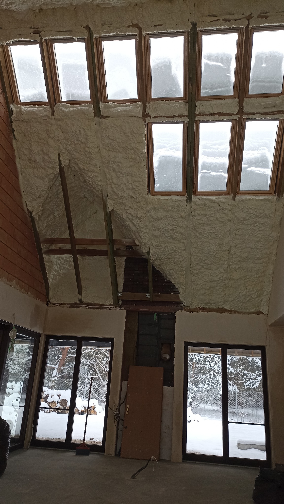 Poddasze z oknami dachowymi, częściowo pokryte pianką izolacyjną, widoczne elementy konstrukcyjne dachu i fragmenty niezabezpieczonej ściany.