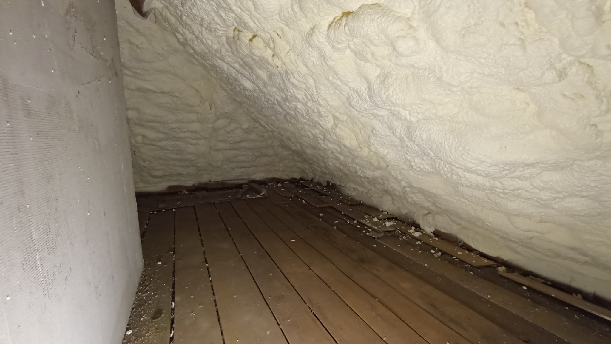 Poddasze po ociepleniu pianką PUR, widoczne nierównomierne pokrycie i fragmenty drewnianej podłogi z resztkami pianki.