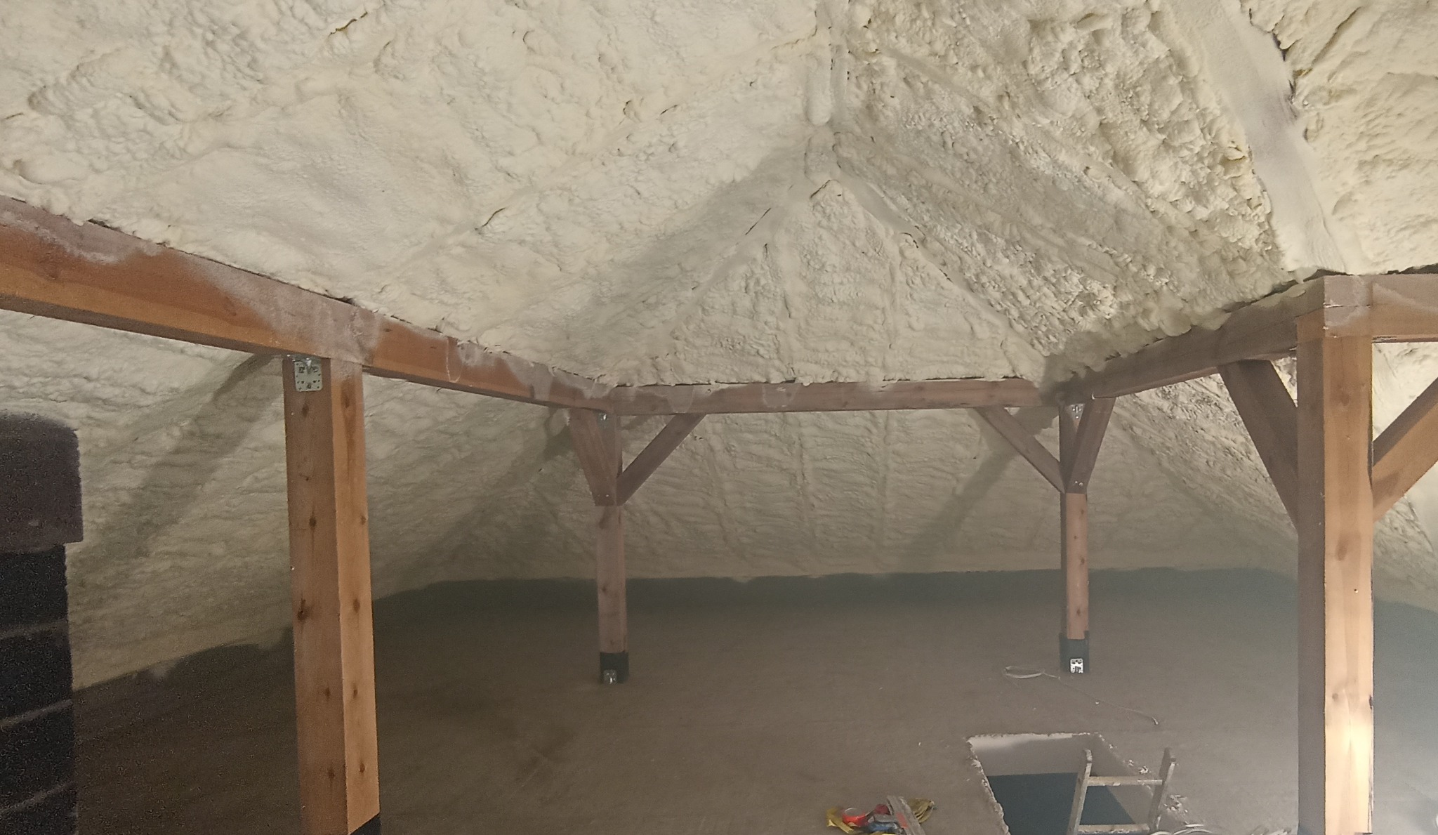 Poddasze z drewnianą konstrukcją pokryte grubą warstwą białej pianki PUR, widoczne fragmenty podłogi i drabiny, oświetlenie tworzy cienie na piance.