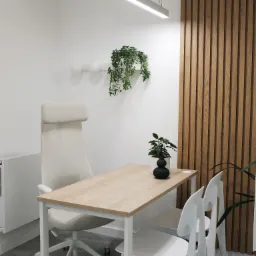 Minimalistyczne biuro z drewnianą ścianą, jasnym biurkiem, ergonomicznym krzesłem i designerskimi lampami.