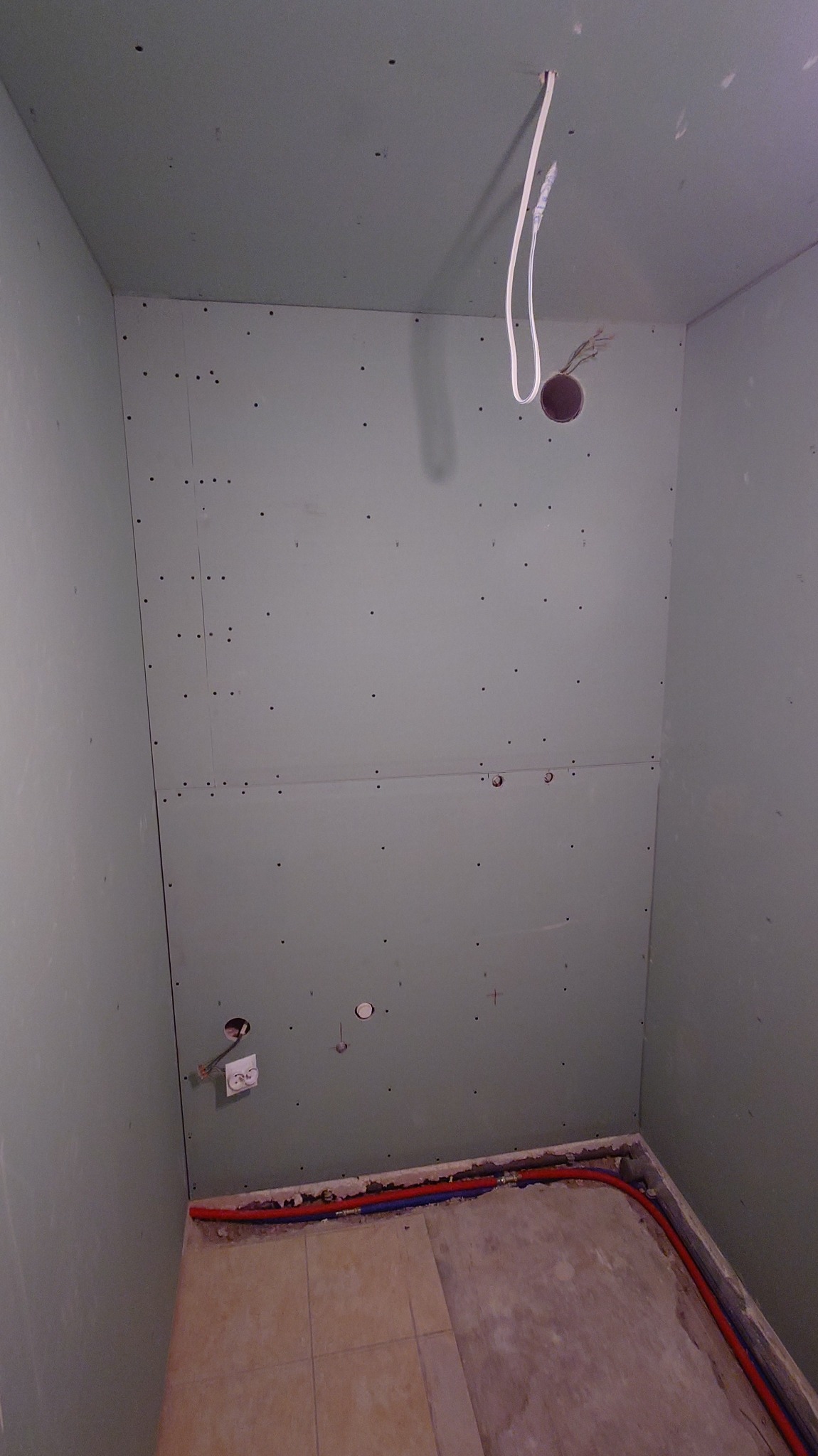 Wnętrze łazienki w trakcie remontu: ściany wyłożone płytami gipsowo-kartonowymi, widoczne instalacje wodne i elektryczne, przygotowane do dalszych prac wykończeniowych.