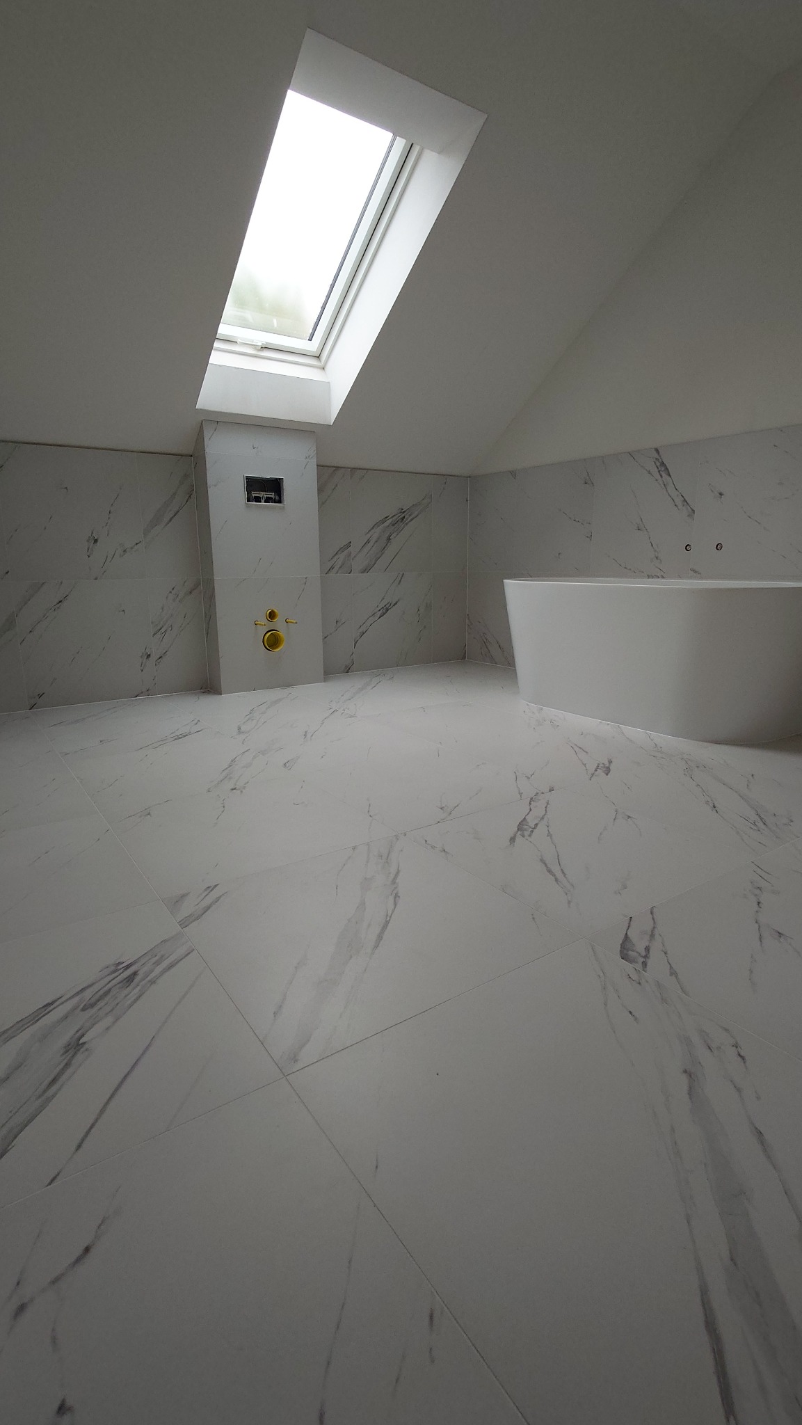 Biała łazienka na poddaszu z marmurowymi płytkami, owalną wanną i oknem dachowym. Minimalistyczny design, widok z góry, podkreślający przestronność i nowoczesny styl.