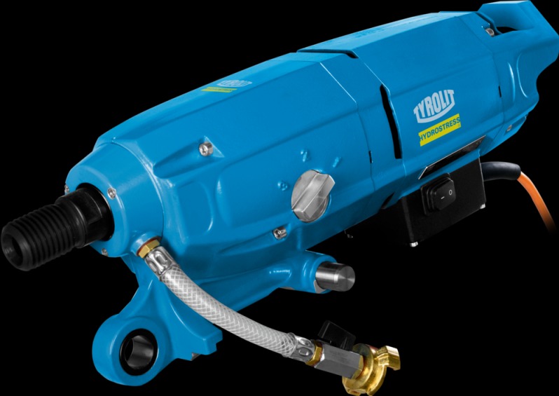 Niebieska wiertnica TYROLIT HYDROSTRESS z podłączonym przewodem wodnym, widoczny włącznik i pokrętło regulacji, na czarnym tle. Sprzęt do wiercenia rdzeniowego.