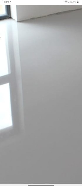 Błyszcząca, gładka, szara posadzka żywiczna z odbiciem okna, widoczna krawędź ściany.