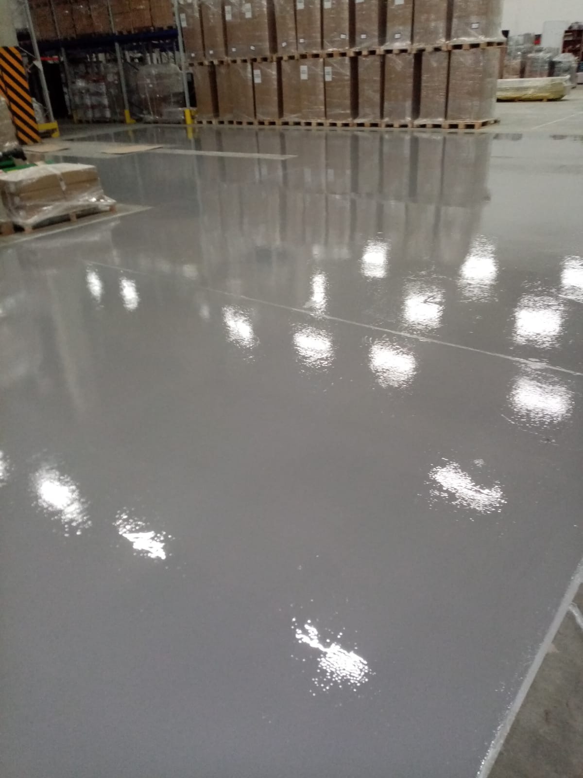 Gładka, szara powierzchnia w hali magazynowej w Sosnowcu, odbijająca światło lamp sufitowych i regały z zapakowanymi towarami.