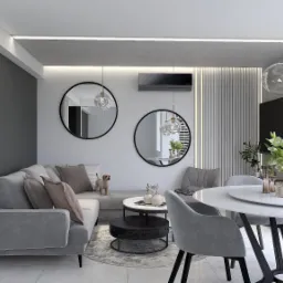 Nowoczesne wnętrze salonu z jadalnią w szarościach, z okrągłym stołem, szklanymi lampami i lustrami, oraz małym psem stojącym na sofie.