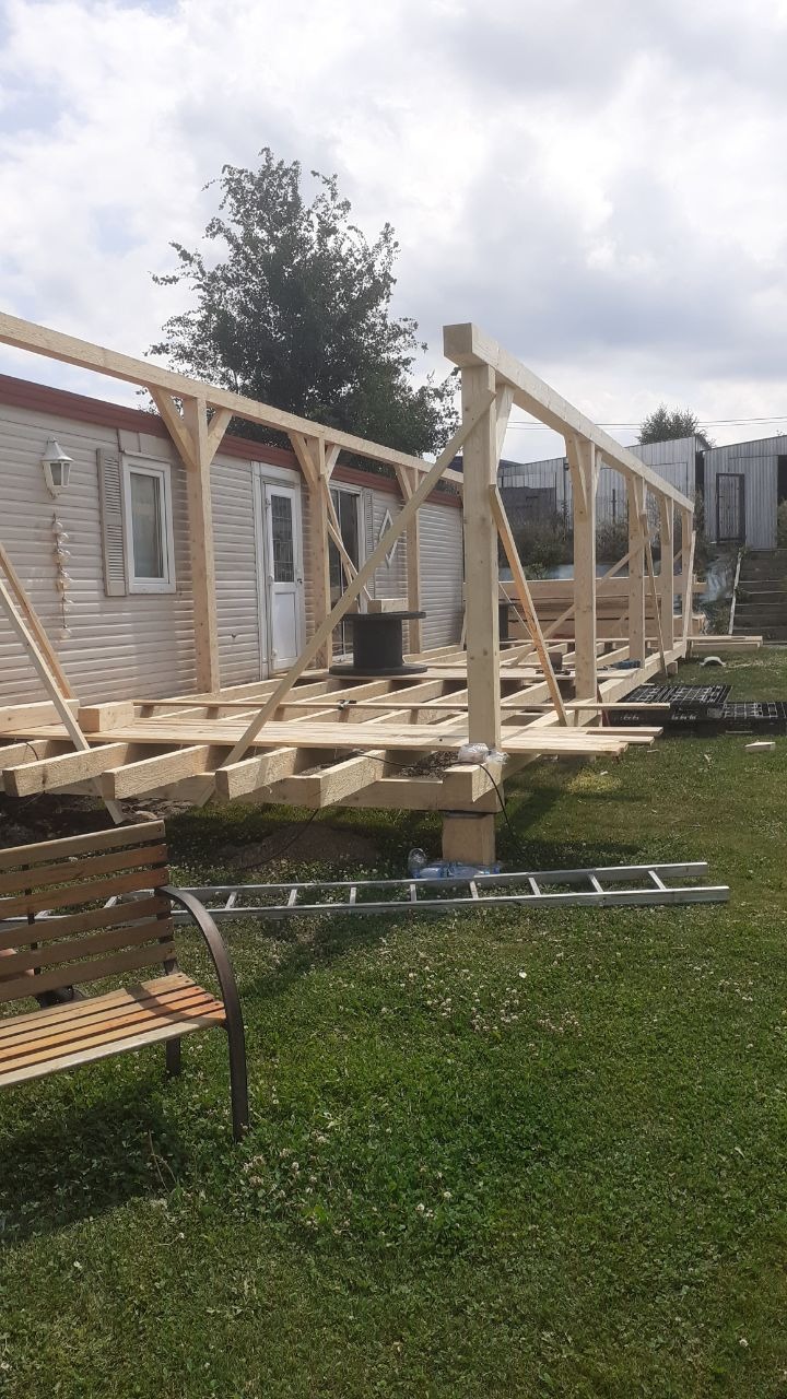 Konstrukcja drewniana w trakcie budowy przylegająca do domu modułowego, widoczna drabina aluminiowa i ławka w ogrodzie.