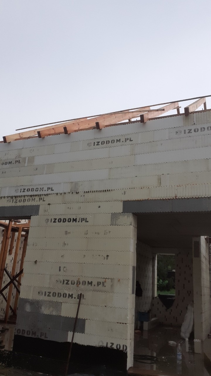 Budowa domu z bloczków IZODOM.PL, widoczna surowa konstrukcja ścian i fragment drewnianej więźby dachowej w trakcie montażu.