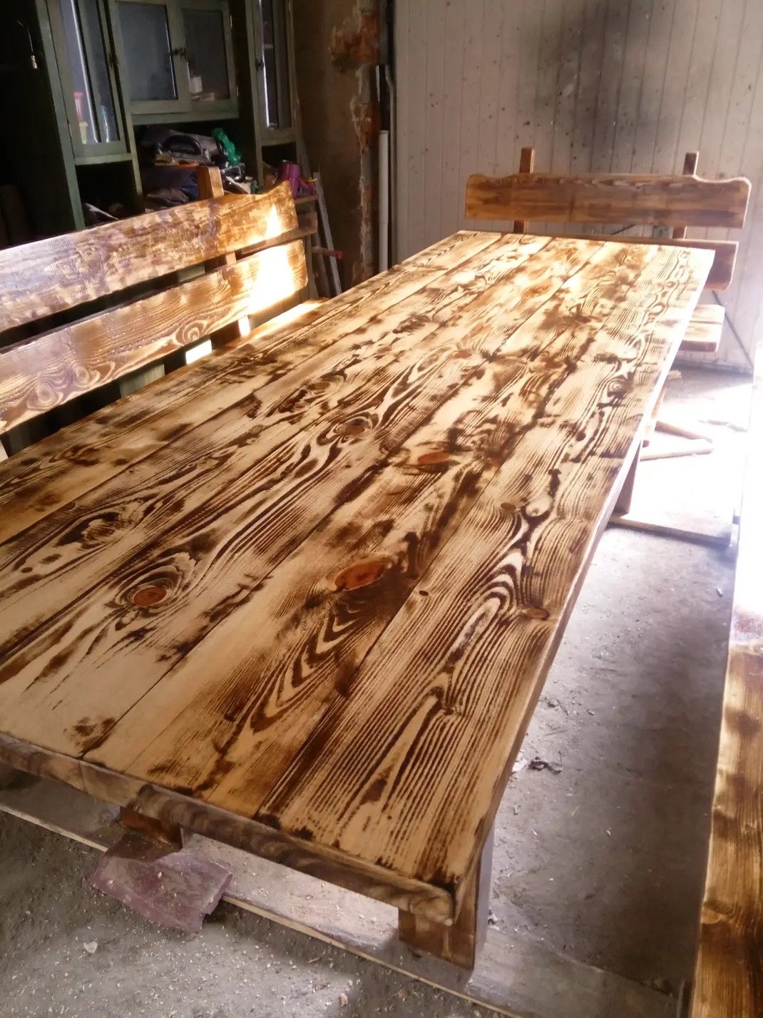 Stół i ławka z surowego drewna z widocznymi słojami, wykończone bejcą w odcieniach brązu, ustawione w warsztacie.