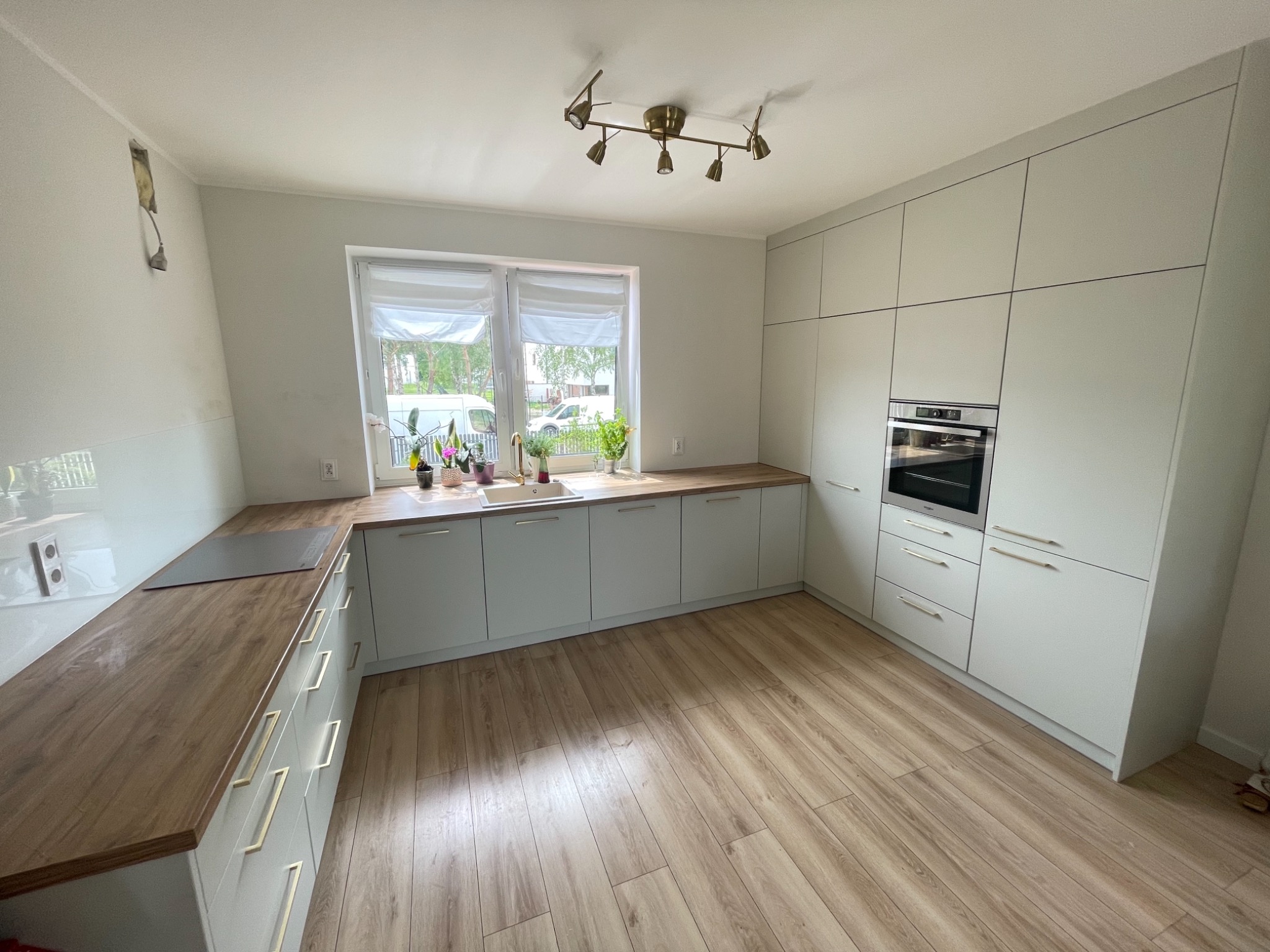 Jasna kuchnia z drewnianym blatem i podłogą, oświetlona lampą sufitową z sześcioma reflektorami, z roślinami w oknie.