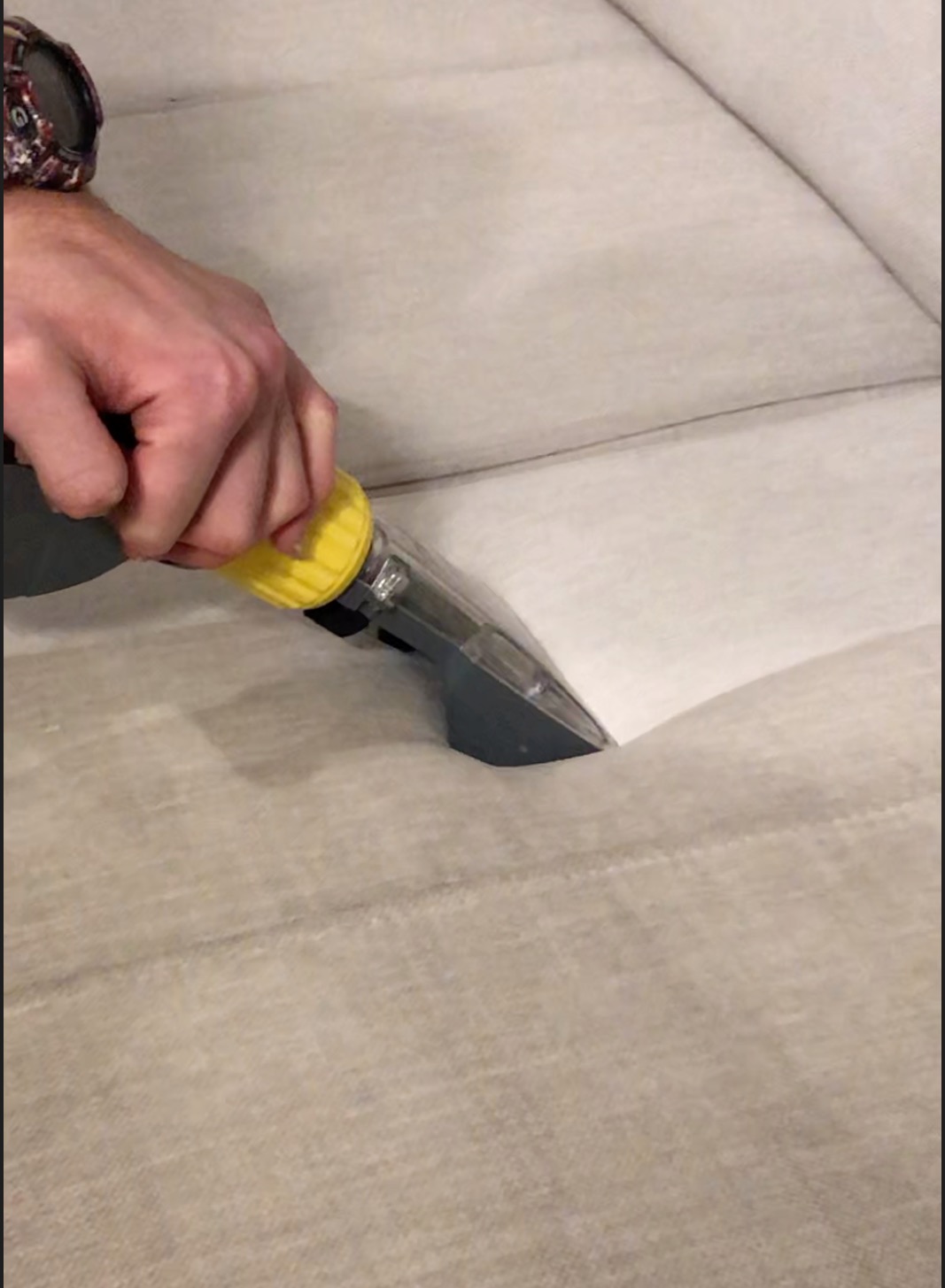 Czyszczenie tapicerki sofy odkurzaczem piorącym, widoczna różnica w kolorze po czyszczeniu, ręka w zegarku.