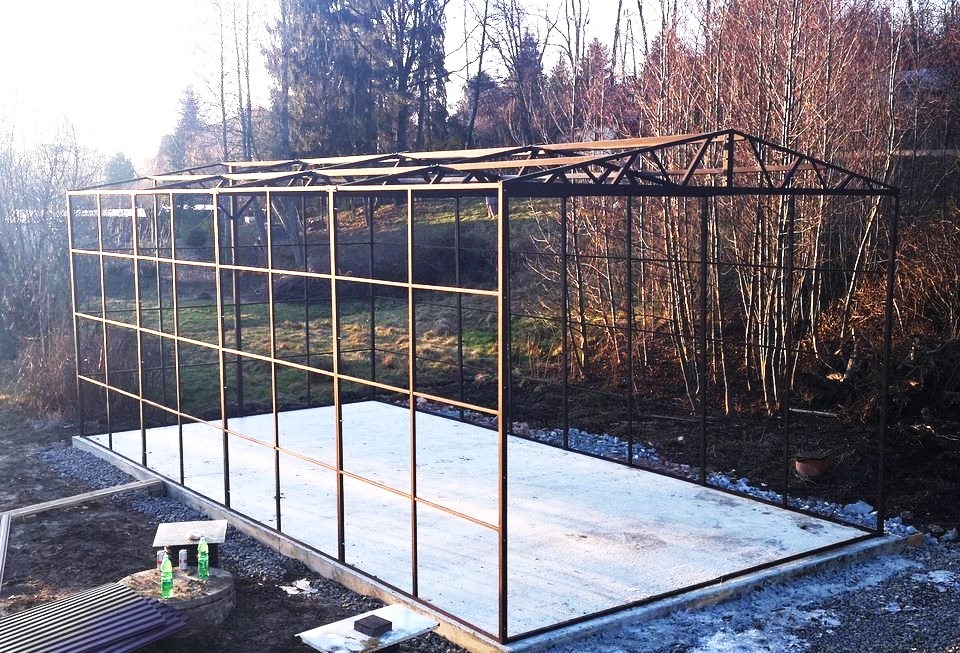 Szkielet stalowej konstrukcji hali w Wirach, widoczny betonowy fundament i otaczający krajobraz z drzewami.