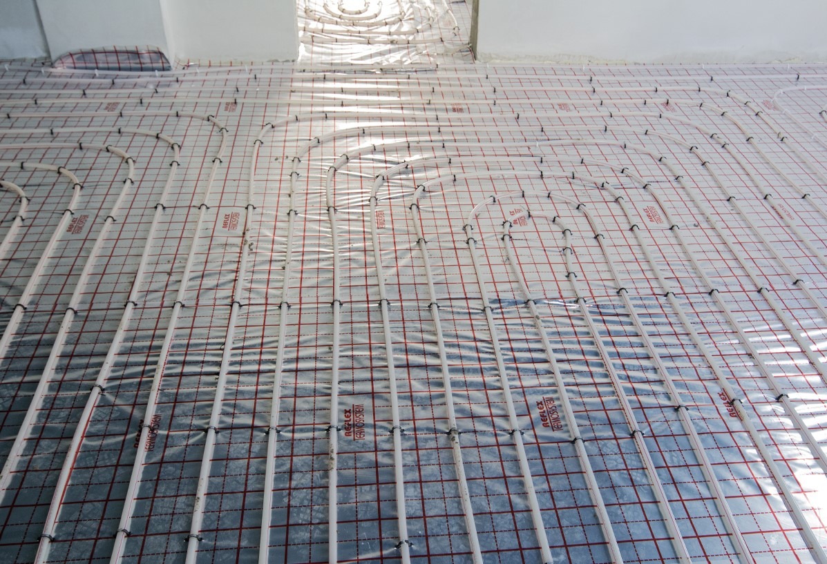 Rozłożone rury ogrzewania podłogowego na folii z siatką, widok z góry, przygotowanie do wylewki.