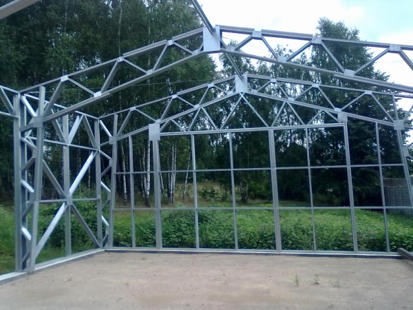 Konstrukcja stalowa hali w trakcie montażu, widoczne kratownice i słupy, tło stanowią drzewa i trawa.